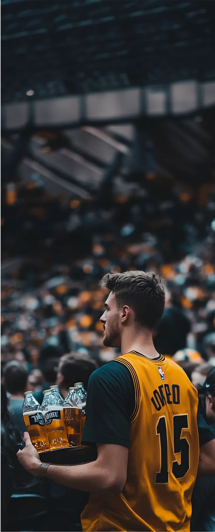 A man wearing a yellow jersey with the number 15, carrying a tray of drinks, standing among a crowd in a stadium