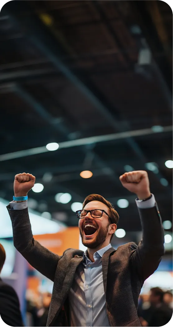 A man in a suit and glasses raising his arms in triumph, expressing joy at an event in a large hall