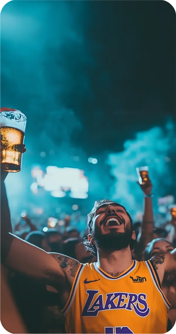 A man wearing a Lakers jersey holding up a pint of beer, celebrating in a crowd during a nighttime event