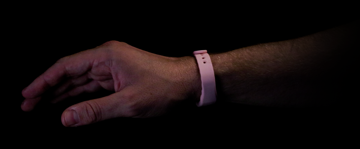 A hand wearing a pink wristband with the 'ryst' logo, on a black background